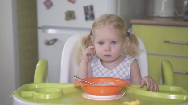 Verdrietig meisje zit aan de tafel met een bord havermoutpap. — Stockvideo