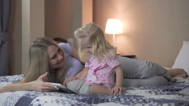 Una madre con un niño con una tableta en el dormitorio en la cama . — Vídeos de Stock