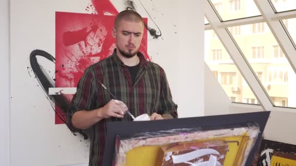 Joven artista moderno hombre pinta un cuadro en el estudio . — Vídeos de Stock
