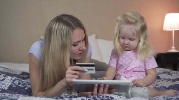 Una mujer enseña a un niño a hacer compras en línea con tarjeta de crédito . — Vídeos de Stock