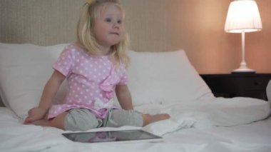 Mutlu küçük kız yatakta bir tablet bilgisayar ile akşam.