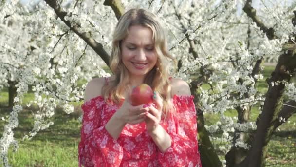 Ung kvinne som spiser et eple i bakgrunnen av blomstrende epletrær . – stockvideo