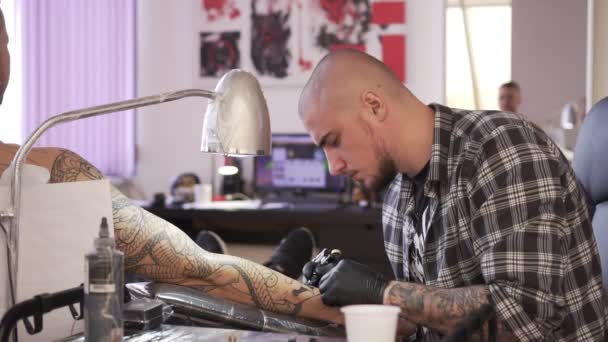 Tatuagem masculina desenha uma tatuagem no braço dos clientes . — Vídeo de Stock
