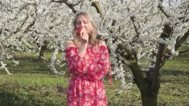 Bahar, elbiseli genç bir kadın doğada bir elma yiyor.