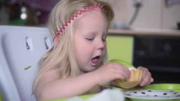 Маленька дівчинка їсть кекс на кухні, повільний рух . — стокове відео