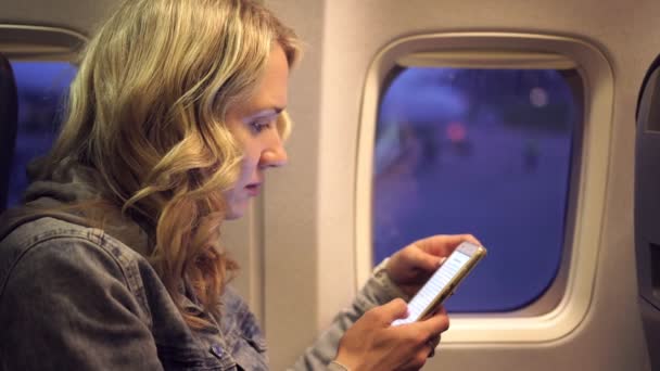 Una joven en un avión con teléfono. chica en el avión con un teléfono inteligente . — Vídeos de Stock