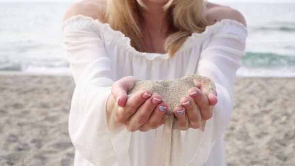 En kvinna håller sand i handflatorna, sand häller genom fingrarna. — Stockvideo