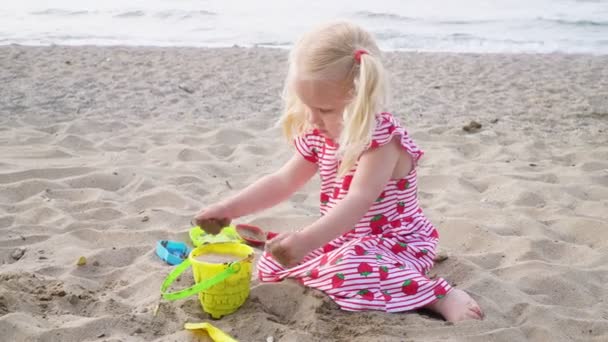 Niña rubia juega en la playa de arena del mar . — Vídeos de Stock