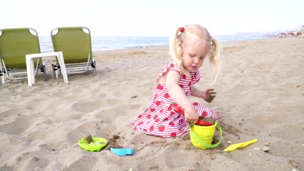 Niña jugando en una playa de arena con una cuchara y un cubo . — Vídeos de Stock