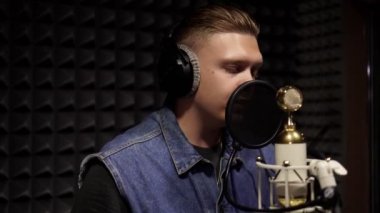 Beyaz adam bir kayıt stüdyosundaki mikrofonda rap okuyor..