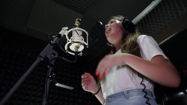 Uma mulher canta em um microfone em um estúdio de gravação . — Vídeo de Stock