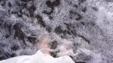 Bir kadın deniz sahilinde siyah kumüzerinde duruyor, bacaklar yakın çekim.