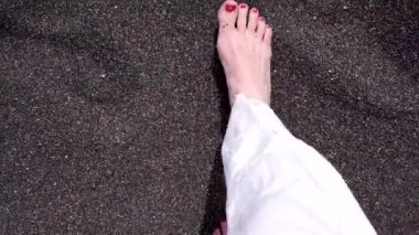 Bir kadın siyah kumda yalınayak yürüyor..