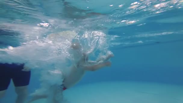 Un niño se sumerge en la piscina y aprende a nadar con un entrenador . — Vídeos de Stock