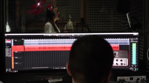Vocal Studios Records. En kvinnlig sångerska sjunger i en mikrofon, ljudteknikern spelar in en låt. — Stockvideo
