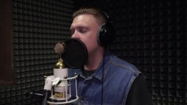 Vokal kayıt stüdyosu. Genç bir adam mikrofona şarkı söyledi..