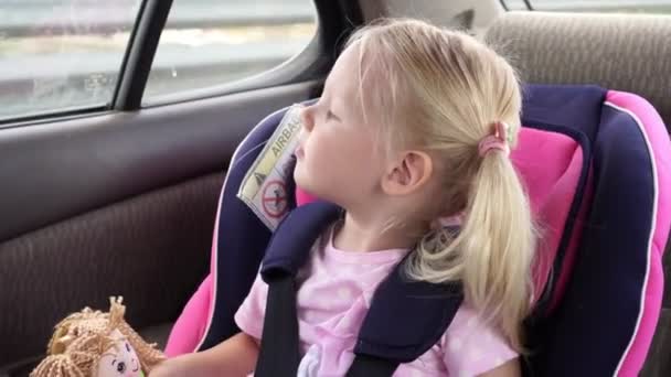 Baby blonde Mädchen fährt in einem Auto in einem Kindersitz. das Kind im Kindersitz. — Stockvideo