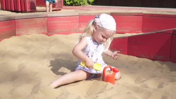 Niña jugando en la caja de arena. Un niño pequeño juega en el verano en la caja de arena . — Vídeos de Stock