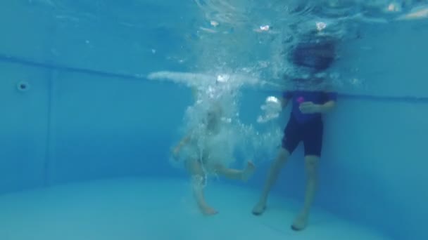 Een gelukkig kind duikt en zwemt in het zwembad onder water. — Stockvideo