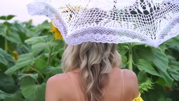 Ung vacker kvinna som går med ett paraply från solen i ett fält av solrosor. — Stockvideo