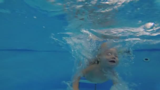 Een klein kind duikt en zwemt onder water in het zwembad. — Stockvideo