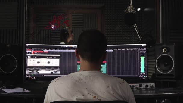 A male sound engineer is recording an artist in a recording studio. — Stock Video