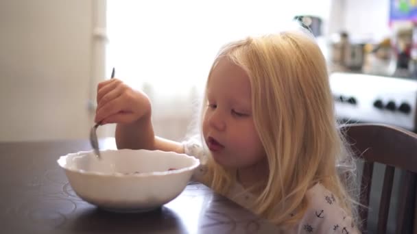 Een meisje eet aan tafel. Klein meisje heeft ontbijt in de keuken. — Stockvideo