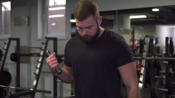 Un hombre está entrenando con pequeñas mancuernas en el gimnasio . — Vídeos de Stock