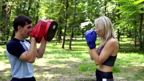 En kvinna boxas i en park med en tränare. — Stockvideo