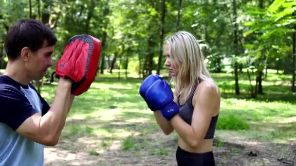 Een vrouw met bokshandschoenen traint met een bokstrainer. — Stockvideo