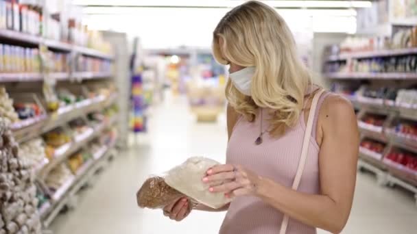 Egy nő egy szupermarketben orvosi maszkban. Védőmaszkos lány egy boltban. — Stock videók