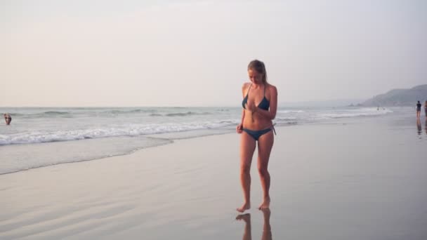 Jonge mooie vrouw in een bikini loopt blootsvoets op het zand aan de zee strand — Stockvideo