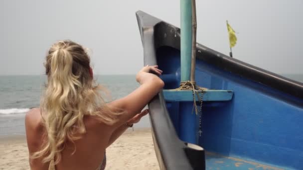 Ung kvinna på bakgrunden av en fiskebåt på stranden — Stockvideo