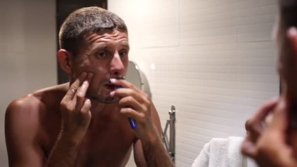 Портрет мужчины, который бреется в ванной перед зеркалом — стоковое видео