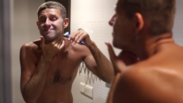 Молодой человек бреется в ванной перед зеркалом. — стоковое видео