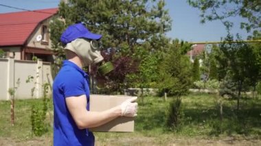 Gaz maskeli bir erkek kurye etrafta dolanıp bir paket teslim ediyor.