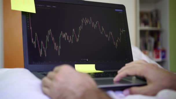 Een man kijkt naar een laptop beurs grafiek. Investeren vanuit huis — Stockvideo