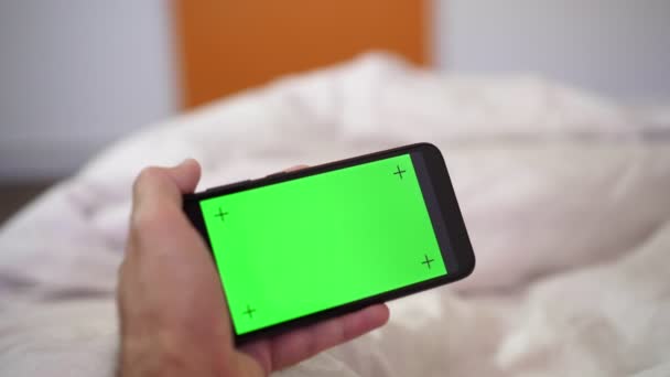 De man thuis gebruikt een smartphone met een blanco groen scherm. — Stockvideo