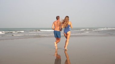 Genç bir çift sabahın köründe kumsalda çıplak ayakla koşuyor.