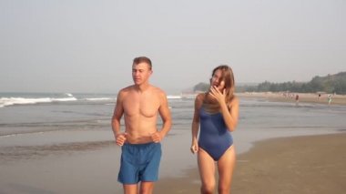 Genç atletik çift deniz kumsalında koşuyor. Kız ve erkek koşuyor.