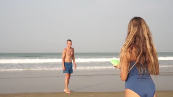 Een jong mooi paar spelen een vliegende schijf of schotel op het strand, slow motion — Stockvideo