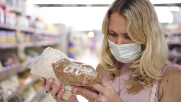 Shopper γυναίκα σε ιατρική μάσκα σε ένα σούπερ μάρκετ επιλέγει τα προϊόντα — Αρχείο Βίντεο