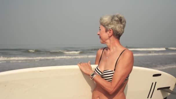 Volwassen aantrekkelijke vrouw in een lied is surfen. Grootmoeder met een surfplank — Stockvideo
