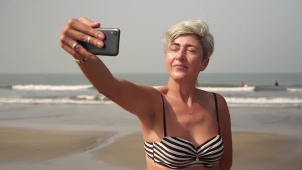 Зрелая женщина делает селфи на смартфоне. Бабушка делает селфи на пляже — стоковое видео