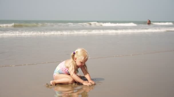 Niña juega en una playa de arena en un fondo del mar. Feliz infancia. . — Vídeo de stock