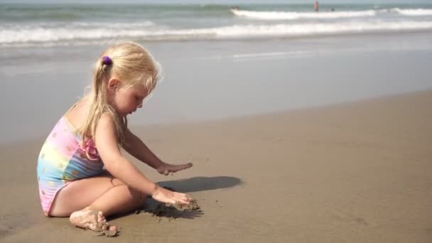 Niño pequeño hermosa chica rubia juega en el mar construye un castillo de arena — Vídeos de Stock