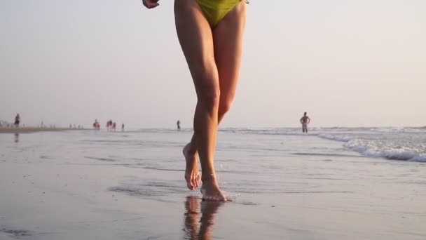 Mayolu bir kadın gün batımına karşı deniz sahilinde koşar, bacakları yakındır. — Stok video