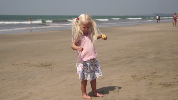 Маленька дівчинка на морському пляжі грає з мильними бульбашками. Дитина з мильними бульбашками — стокове відео