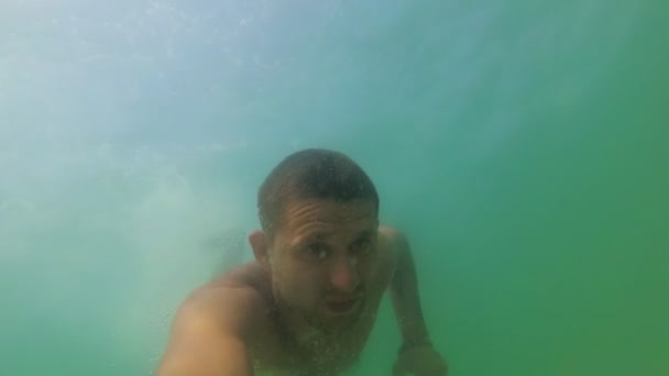 Молодой человек медленно и плавно плавает в море на глубине под водой — стоковое видео
