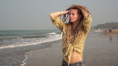 Uzun saçlı genç bir kız kumlu sahil boyunca yürüyor.